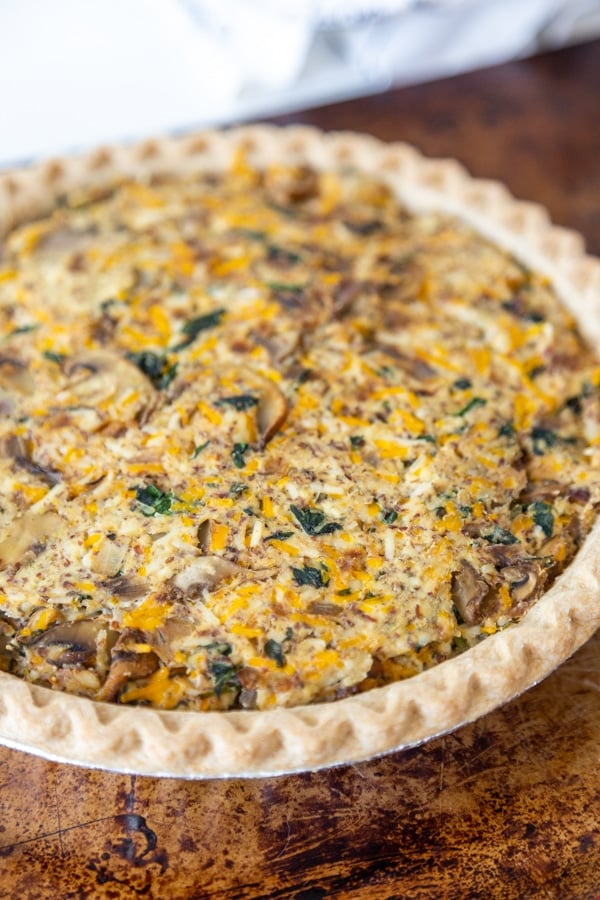 A mushroom and spinach quiche in a pie plate on a metal tray.