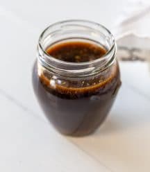 A glass jar filled with Worcestershire sauce on a white wood table.