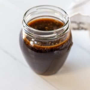 A glass jar filled with Worcestershire sauce on a white wood table.