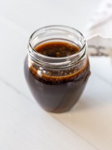 A glass jar filled with Worcestershire sauce on a white wood table.