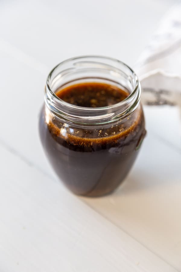 A glass jar filled with Worcestershire sauce on a white wood table.