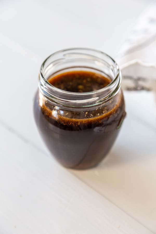 A glass jar filled with Worcestershire sauce on a white wood table. 