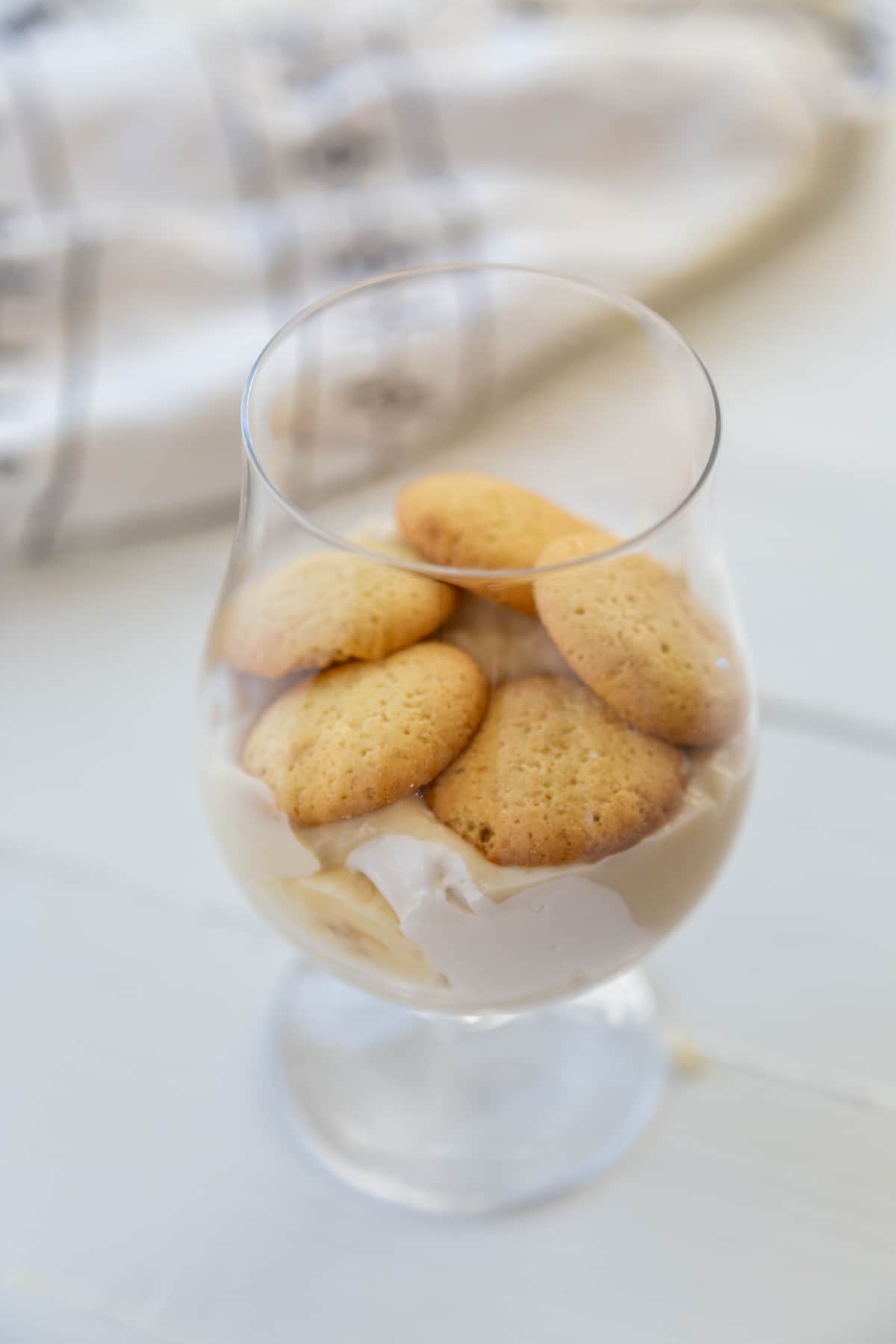 A glass with vanilla pudding, whipped topping, and vanilla wafers.