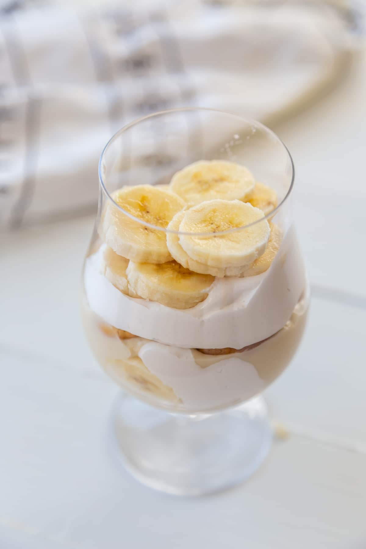 A glass with layers of vanilla wafers, vanilla pudding, whipped topping, and sliced bananas.