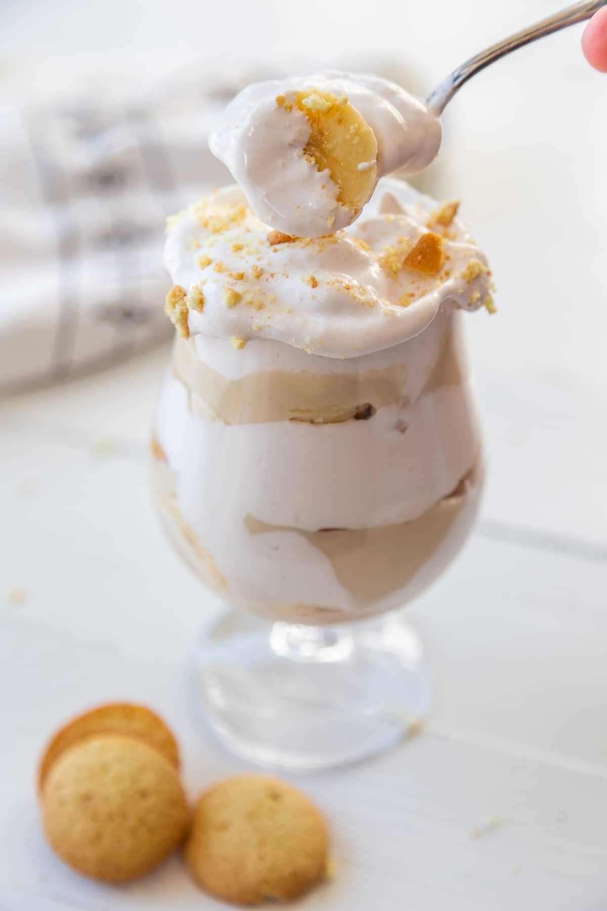 A spoonful of banana pudding over a glass of the dessert and 3 vanilla wafers next to the glass.