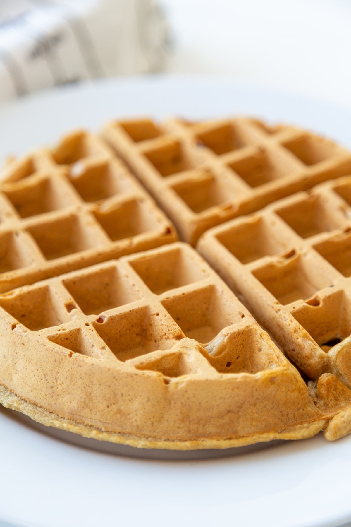 A Belgian waffle on a white plate with a white and black towel behind the plate.