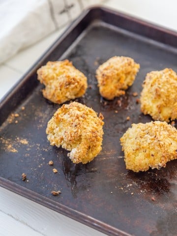 Oven fried breaded cauliflower on a baking sheet with a white and black towel in the background.