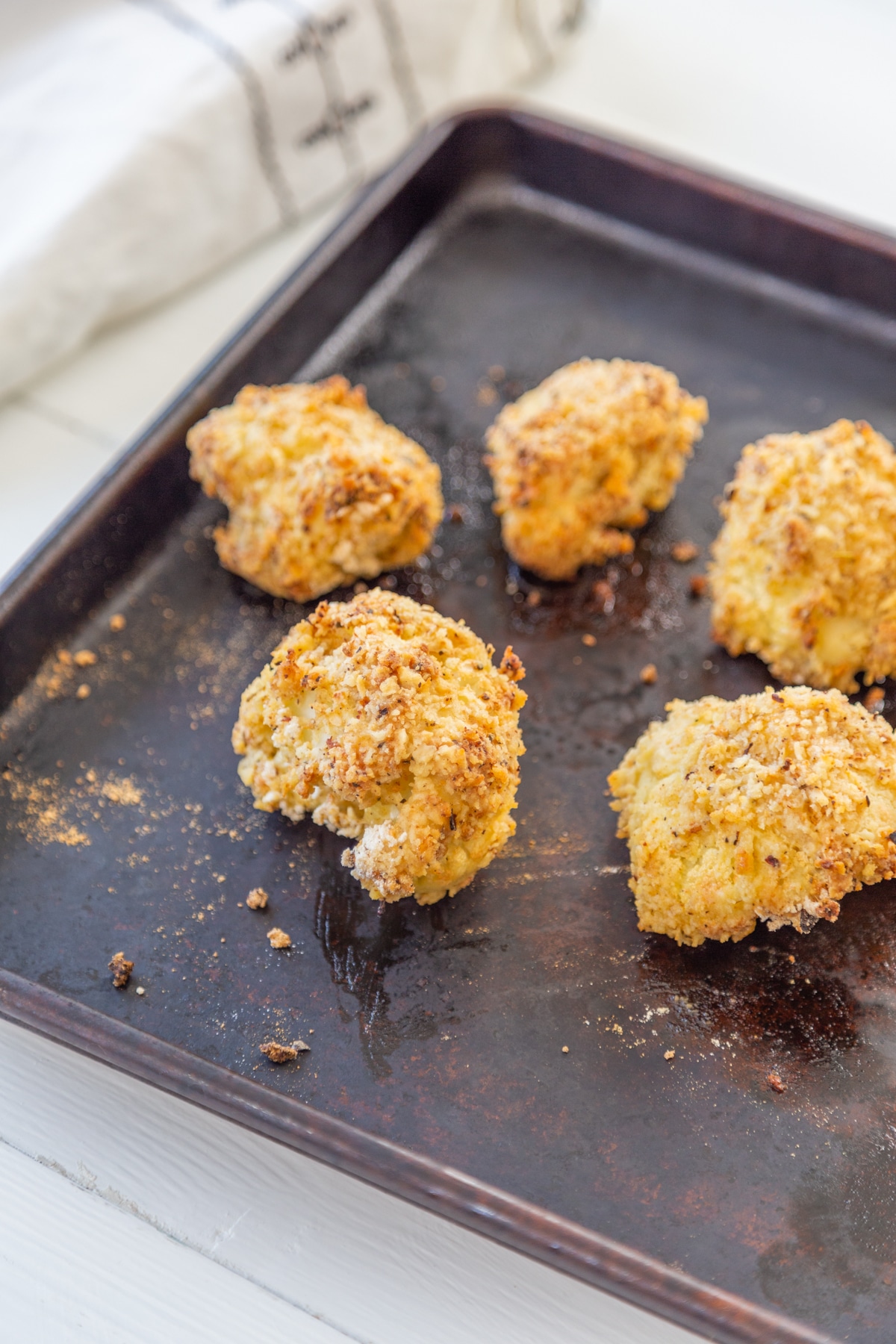 Oven fried breaded cauliflower on a baking sheet with a white and black towel in the background.