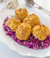 A white scalloped edge plate with a bed or chopped red cabbage with crispy cauliflower on top.