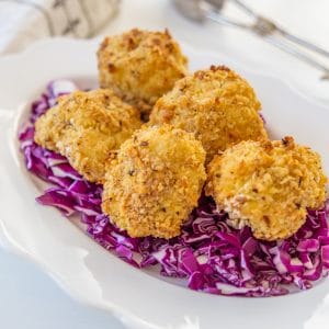 A white scalloped edge plate with a bed or chopped red cabbage with crispy cauliflower on top.