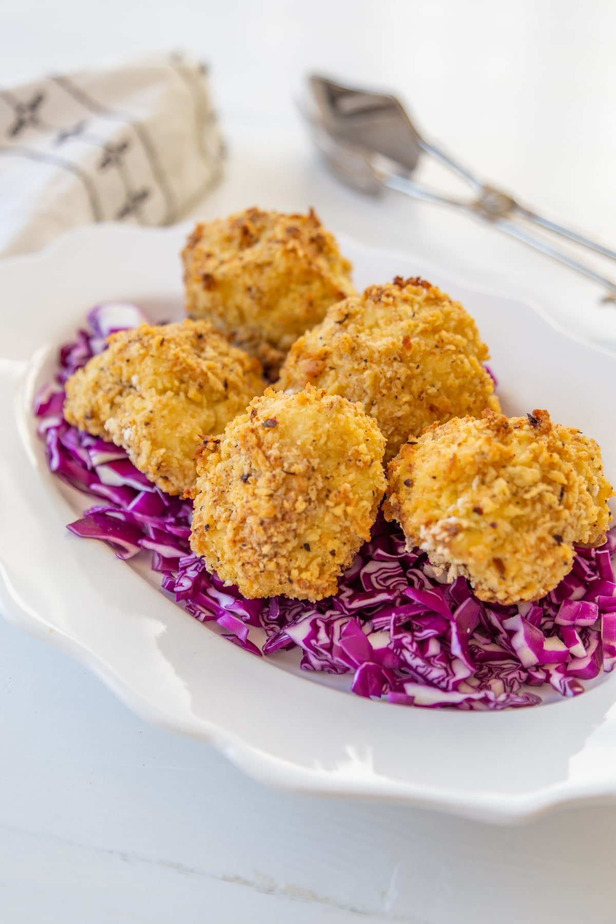 A white scalloped edge plate with a bed or chopped red cabbage with crispy cauliflower on top. 