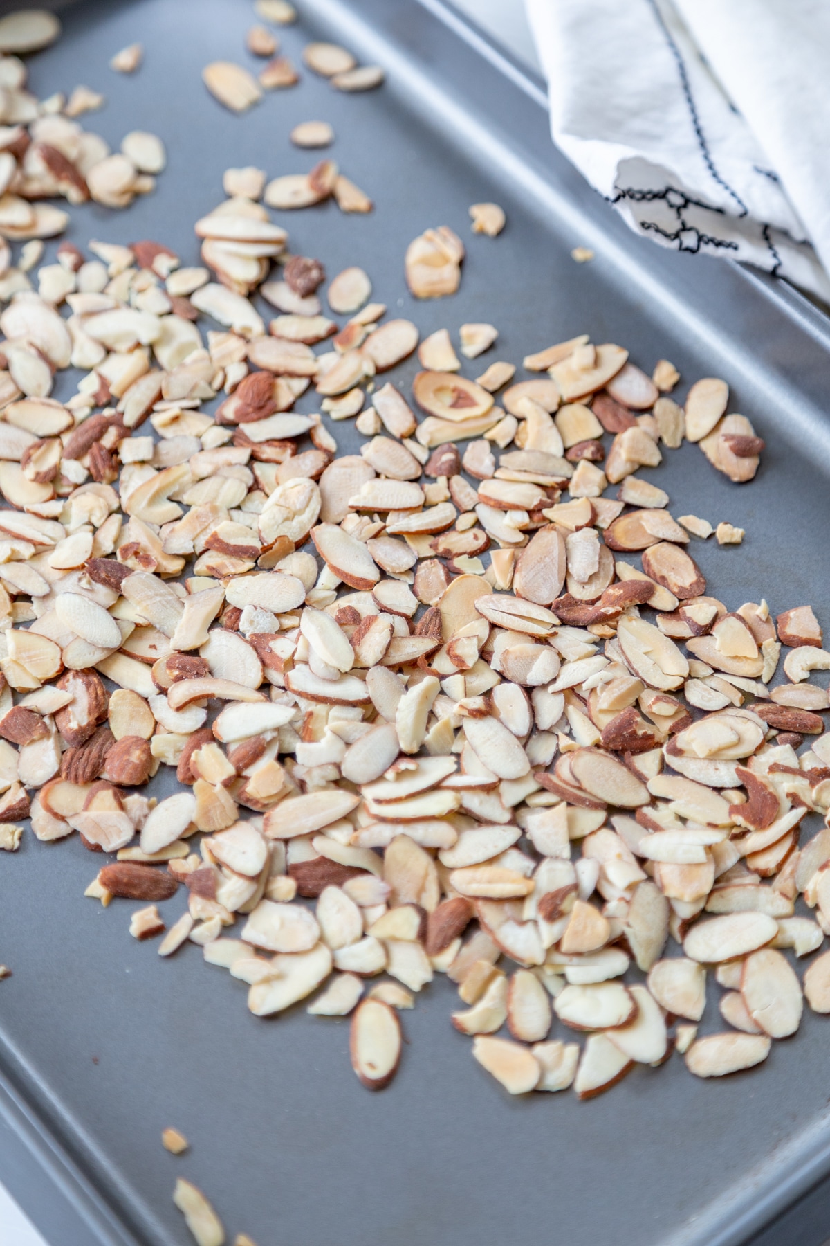 A silver baking pan with slivered almonds spread out on it. 