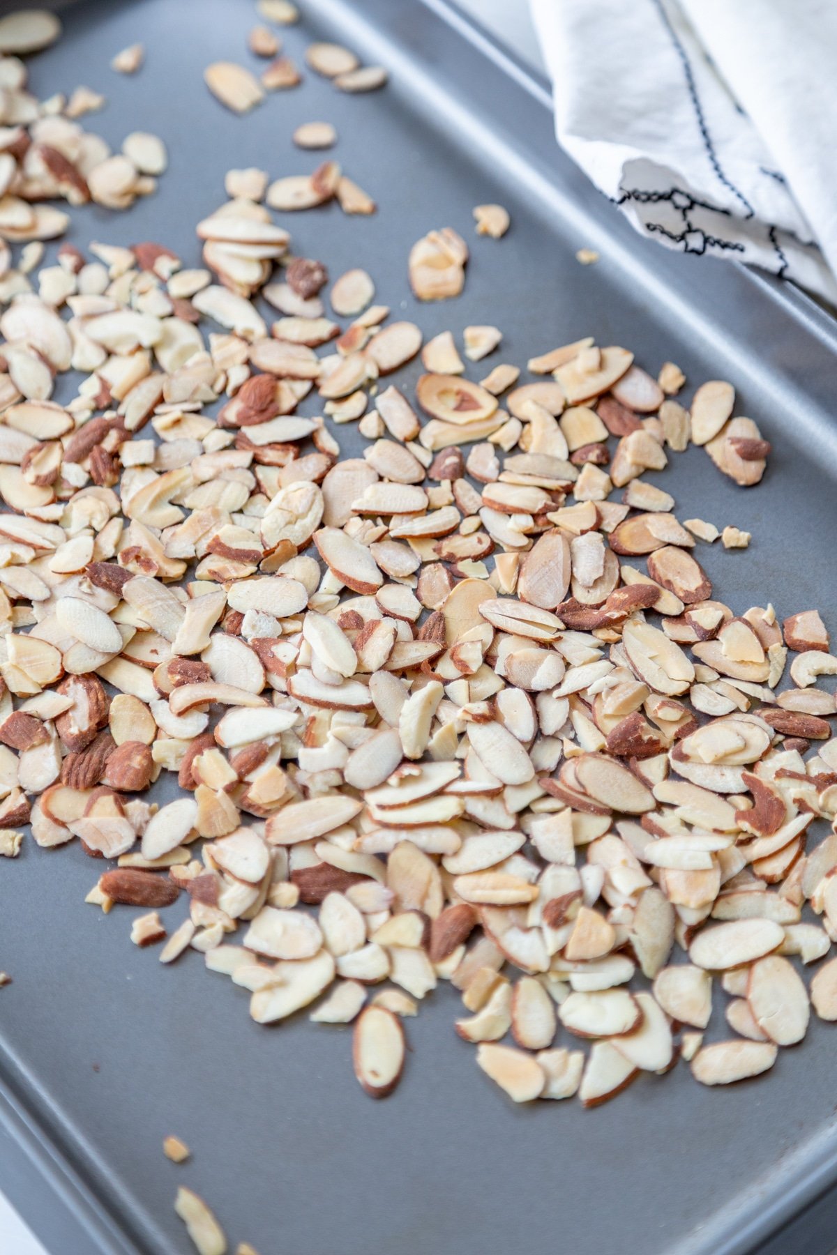 A silver baking pan with slivered almonds spread out on it. 