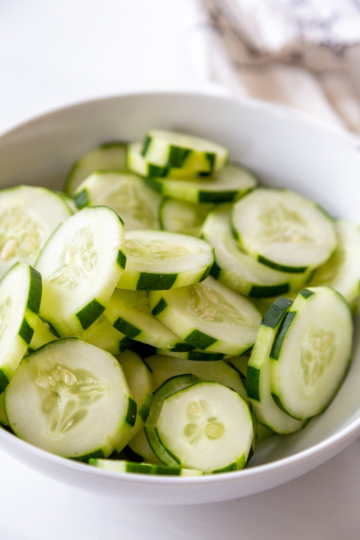 A white bowl full of sliced cucumbers. 