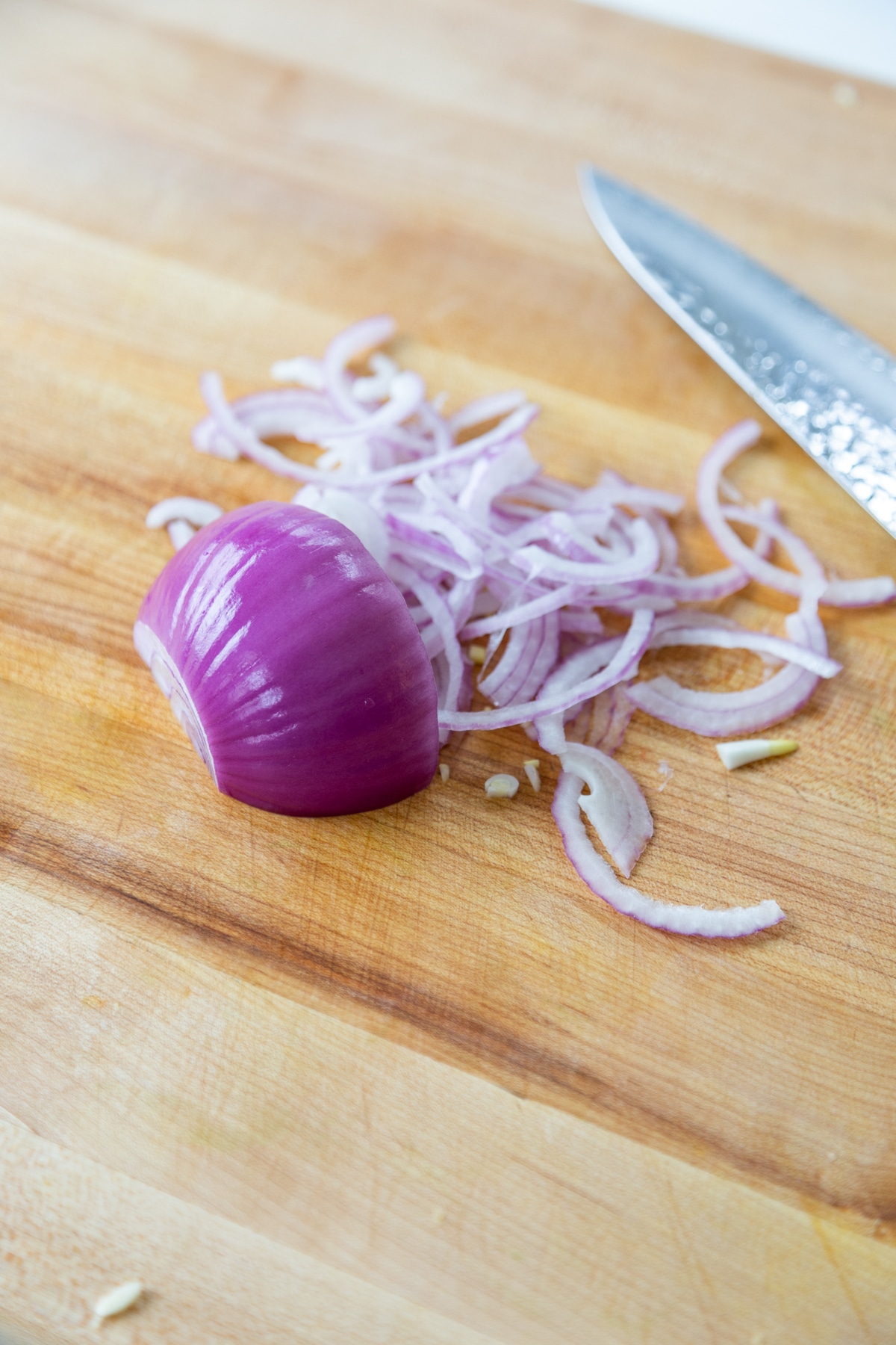 Thinly sliced red onion from half of an onion on a wooden cutting board with a knife on the board.