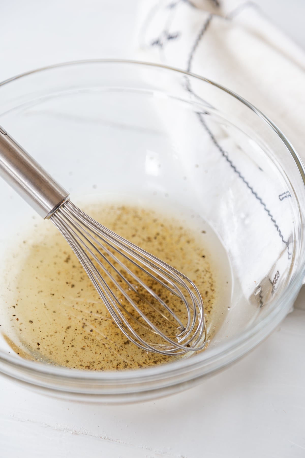 A clear glass bowl with a vinegar salad dressing being whisked with a silver whisk.