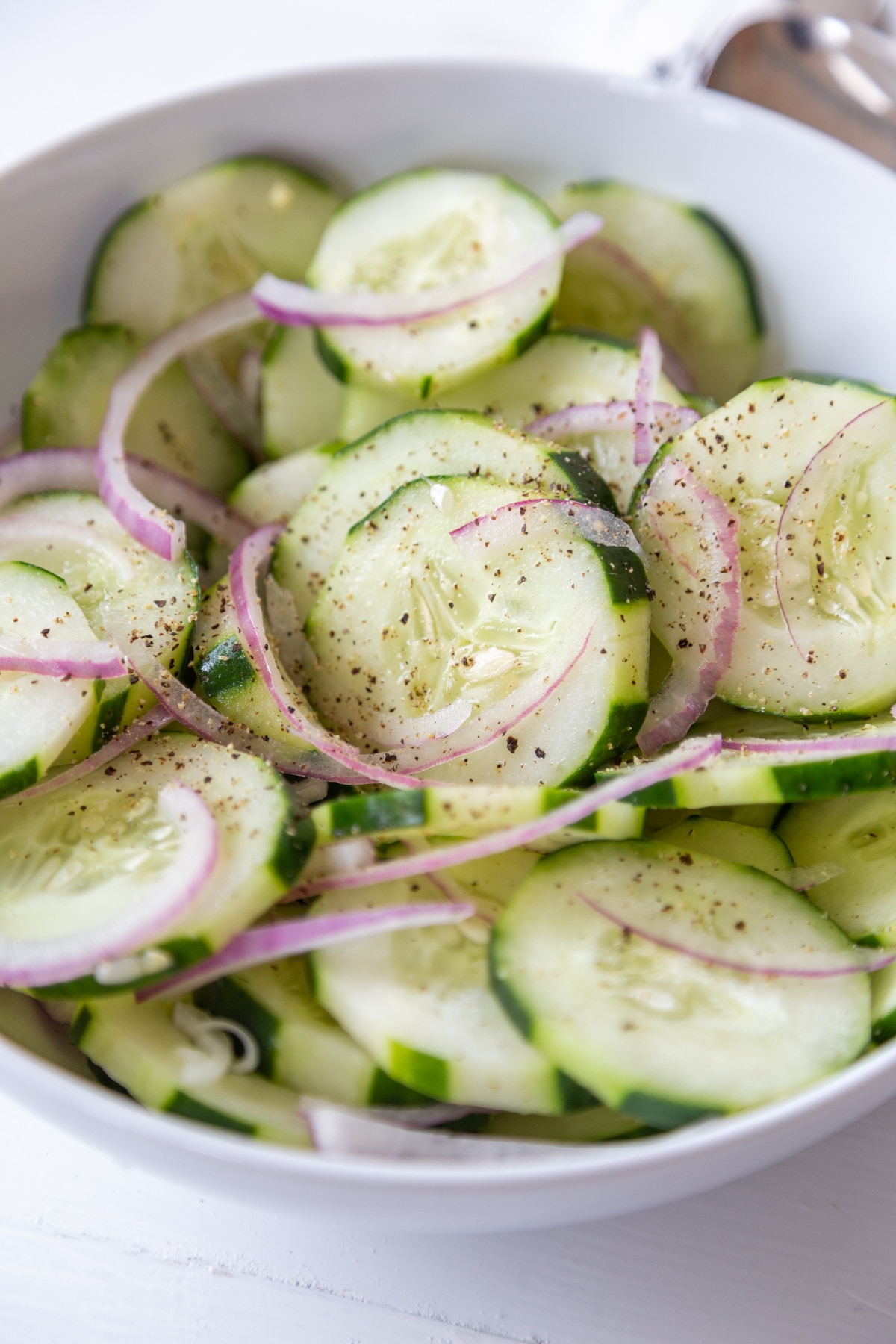 Cucumber and red onion salad in a white bowl being tossed with a silver spoon.