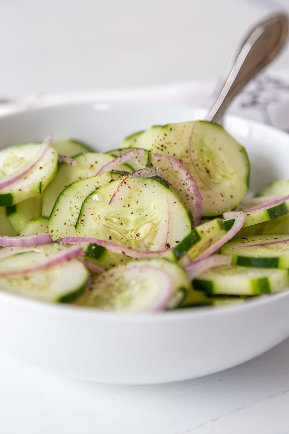 A white bowl filled with cucumber salad with a silver serving spoon in the bowl.