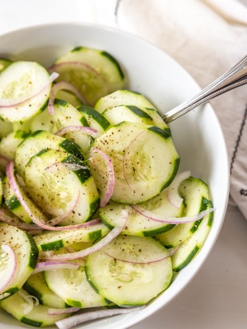A cucumber and red onion salad in a white bowl with a silver spoon in the bowl.