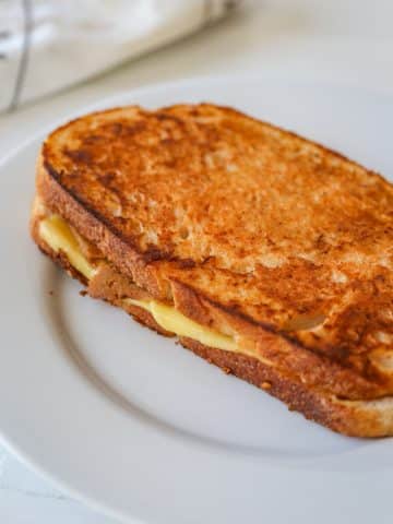 A monte cristo ham and cheese grilled sandwich on a white plate.