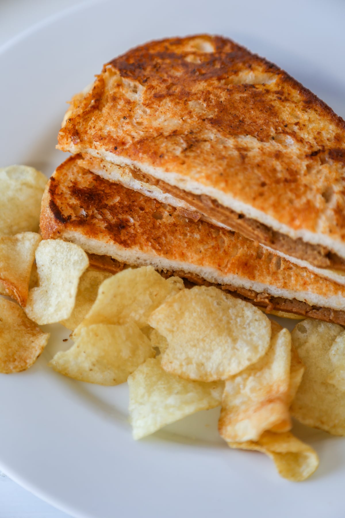 A grilled monte cristo sandwich cut in half in triangles and stacked on a white plate with potato chips. 