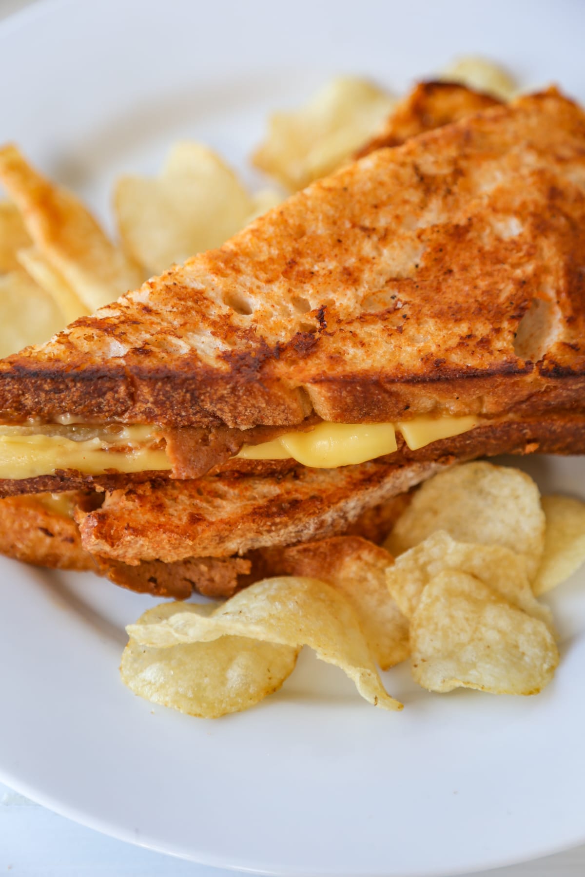 A grilled monte cristo sandwich cut in half in triangles and stacked, with potato chips on a white plate.