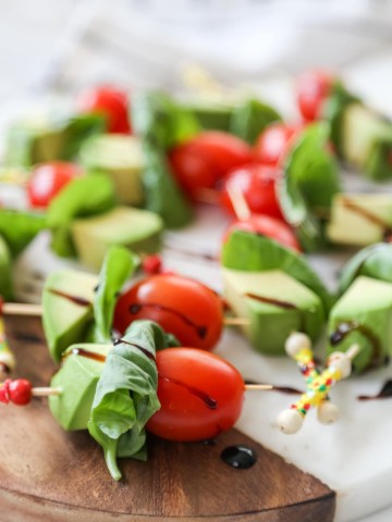 Avocado and tomato skewers with balsamic vinegar on a wood and marble board.