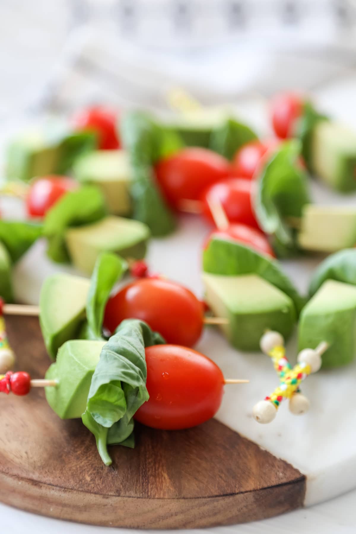 Tomato, basil, and avocado kabobs on a marble and wood board. 