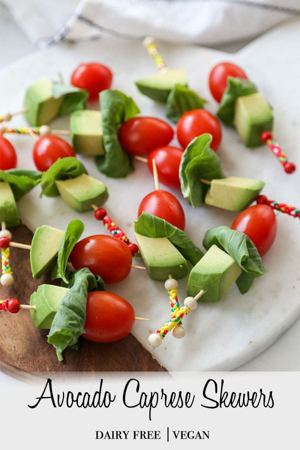 A PInterest pin for avocado caprese skewers with a picture of the skewers on a wood and marble board. 