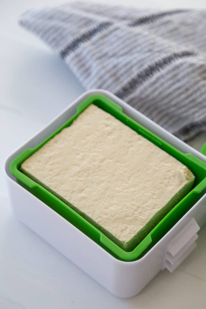 A block of tofu in a green and white tofu press.