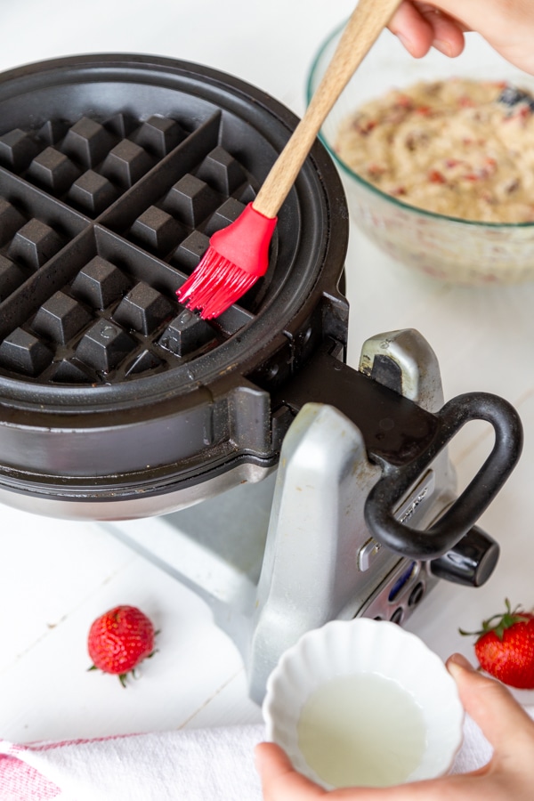 A red silicone pastry brush brushing oil on a waffle iron.