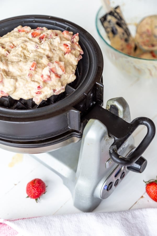 Strawberry pecan waffle batter being spread on a waffle iron.