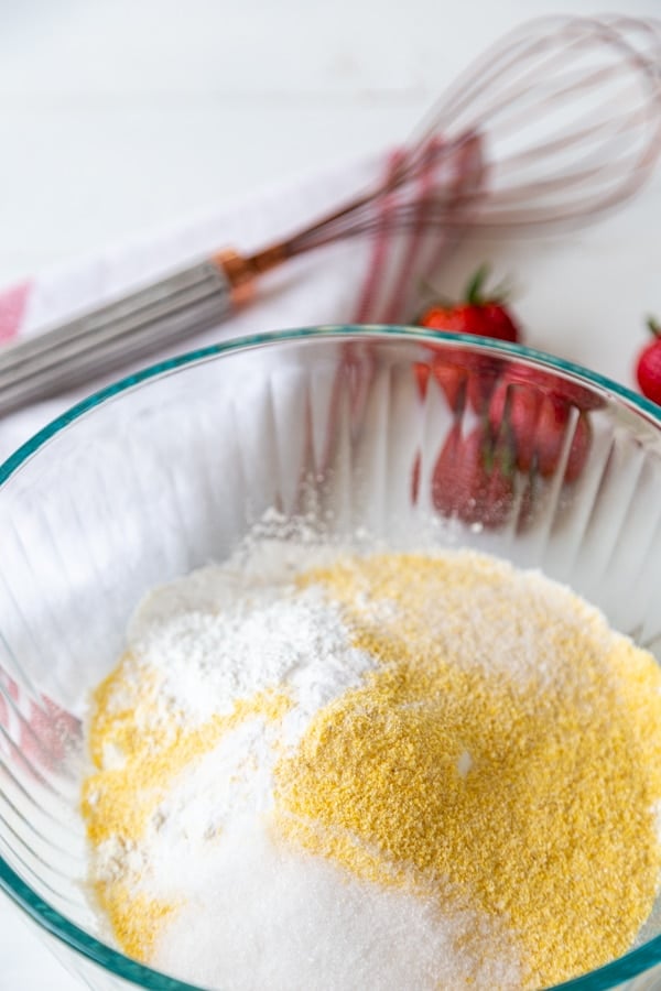 A glass mixing bowl with flour, cornmeal, and sugar.