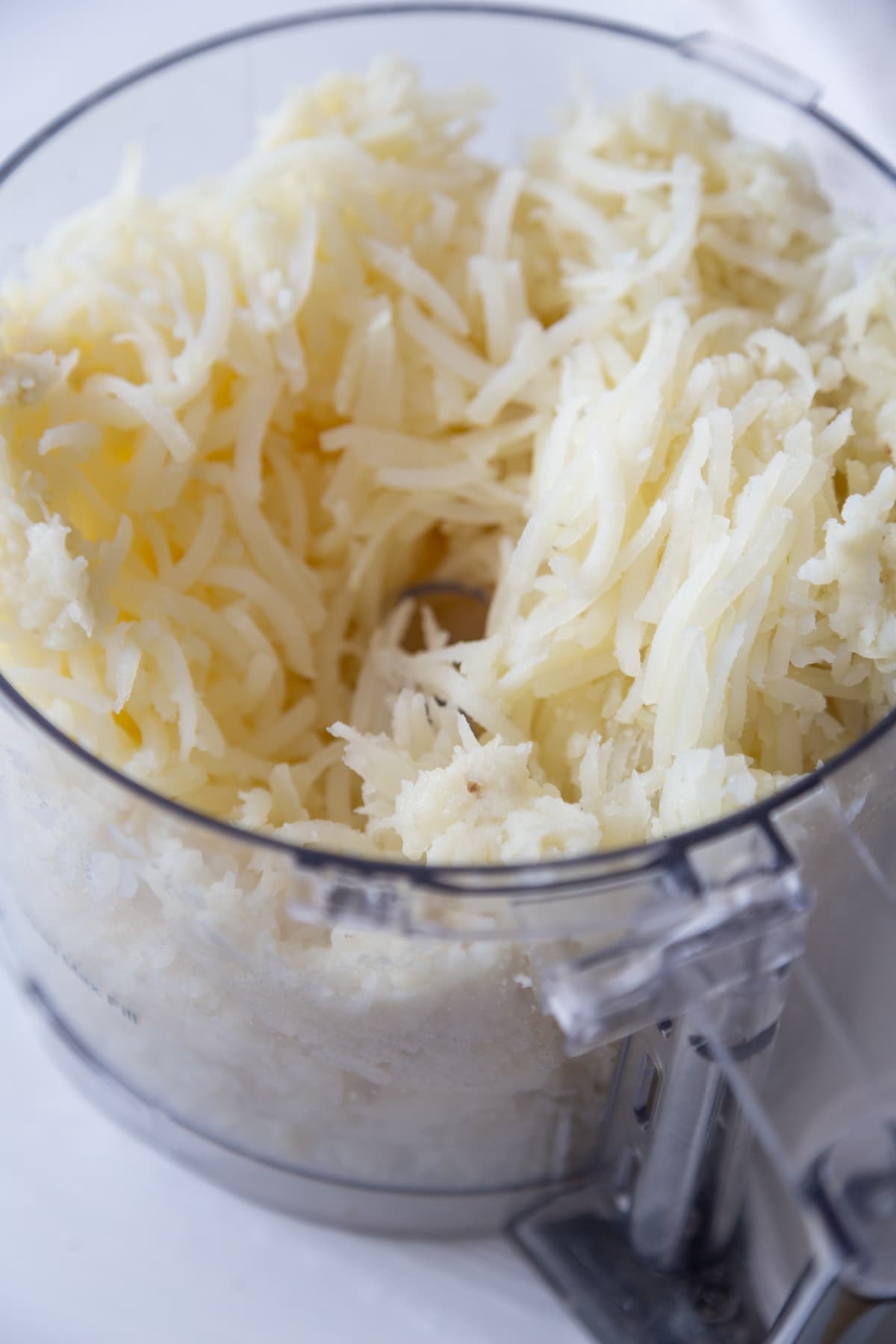 A food processor filled with shredded potato.