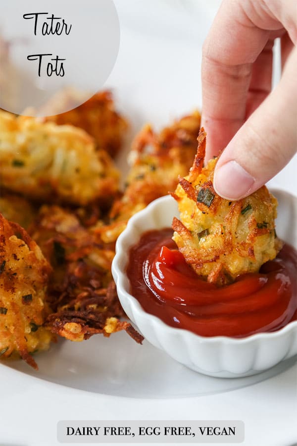 A Pinterest pin for vegan cheesy tater tots with a picture of a hand dipping a tot in a dish of ketchup.