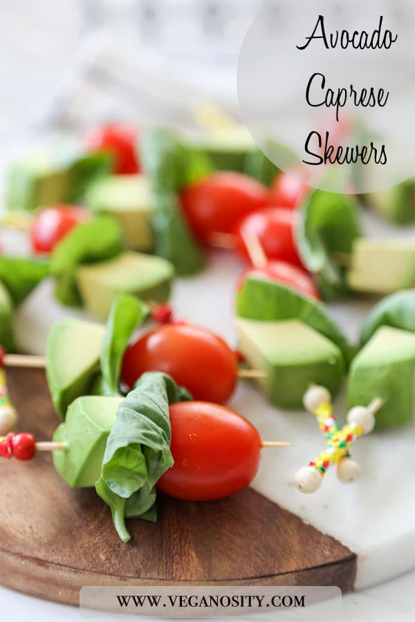 A Pinterest pin with a close up picture of avocado caprese skewers on a wood and marble board.