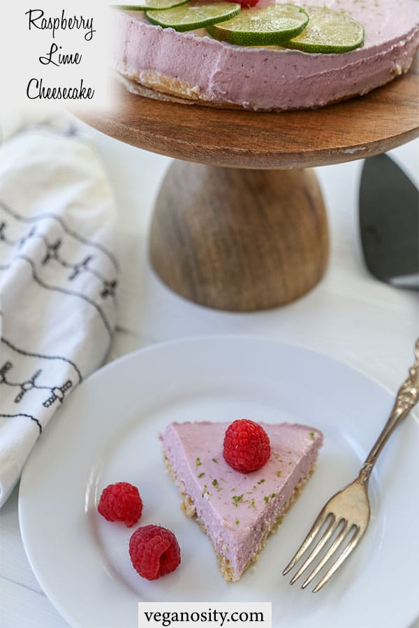A Pinterest pin for raspberry lime cheesecake with a picture of a slice of the cake on a white plate and the whole cake on a wooden cake stand in the background. 