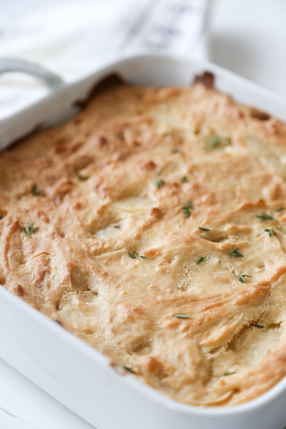 Potatoes au gratin in a square white baking dish with handles, sprinkled with minced thyme.
