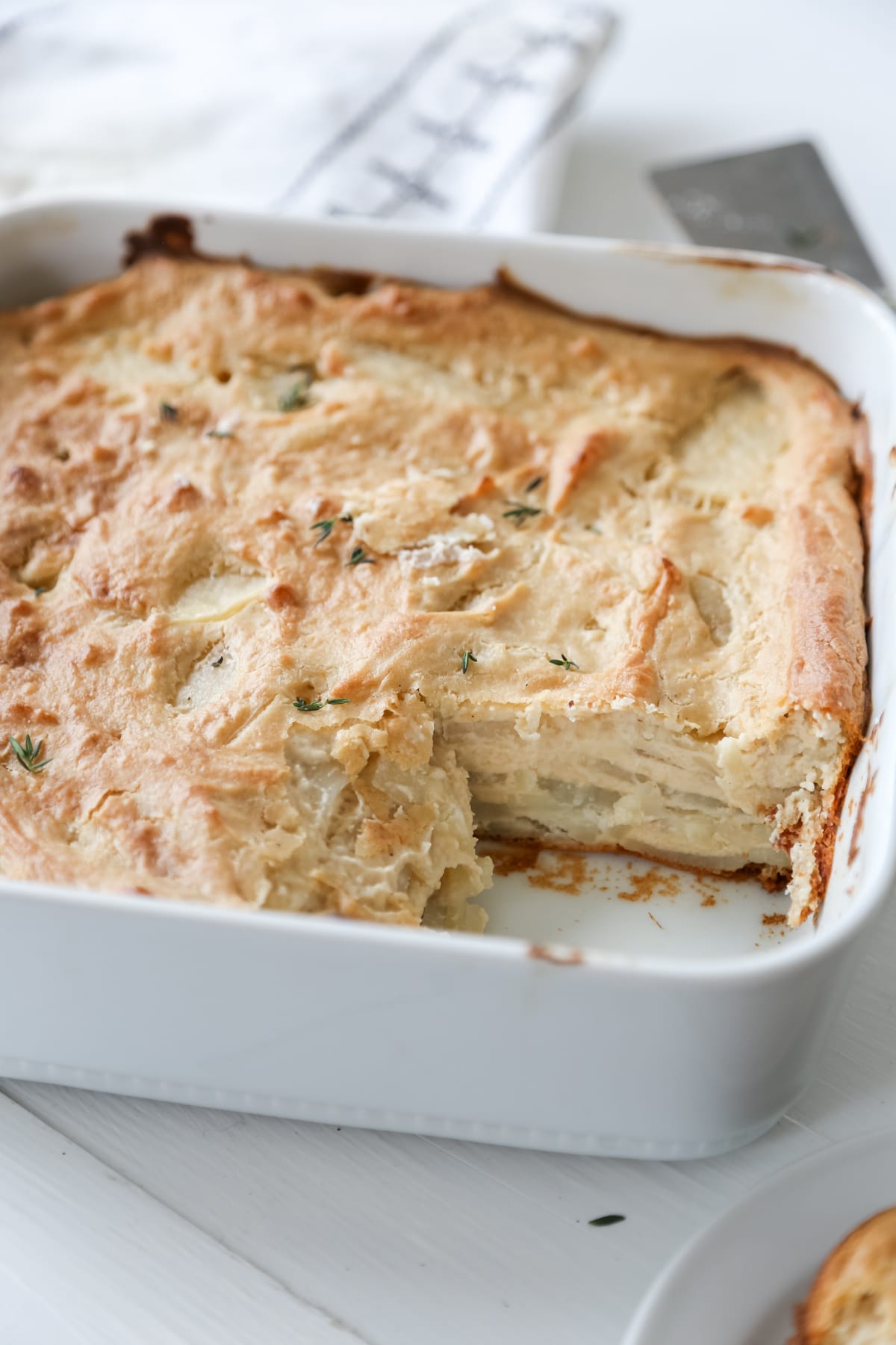 A square white baking dish with potatoes au gratin and a square piece is missing from the pan.