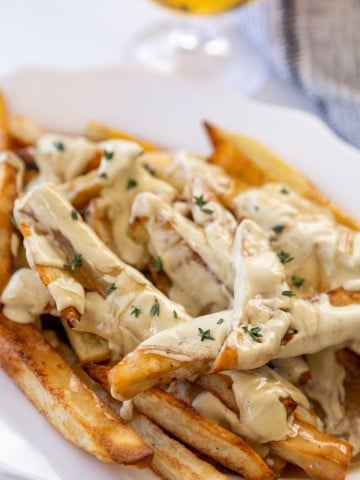 A white oval platter with fries that are covered in cheese sauce and gravy, and sprinkled with thyme leaves.