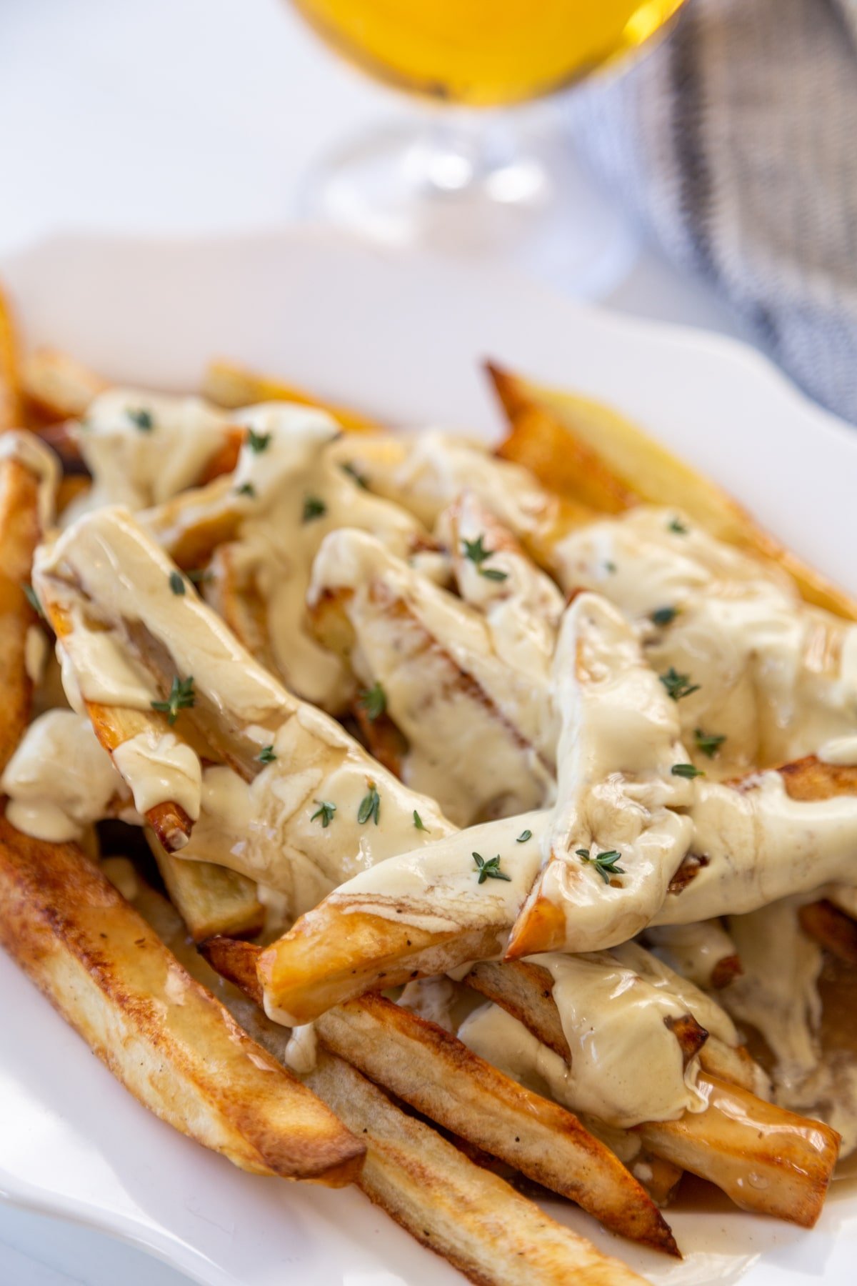 A white oval platter with fries that are covered in cheese sauce and gravy, and sprinkled with minced chives.