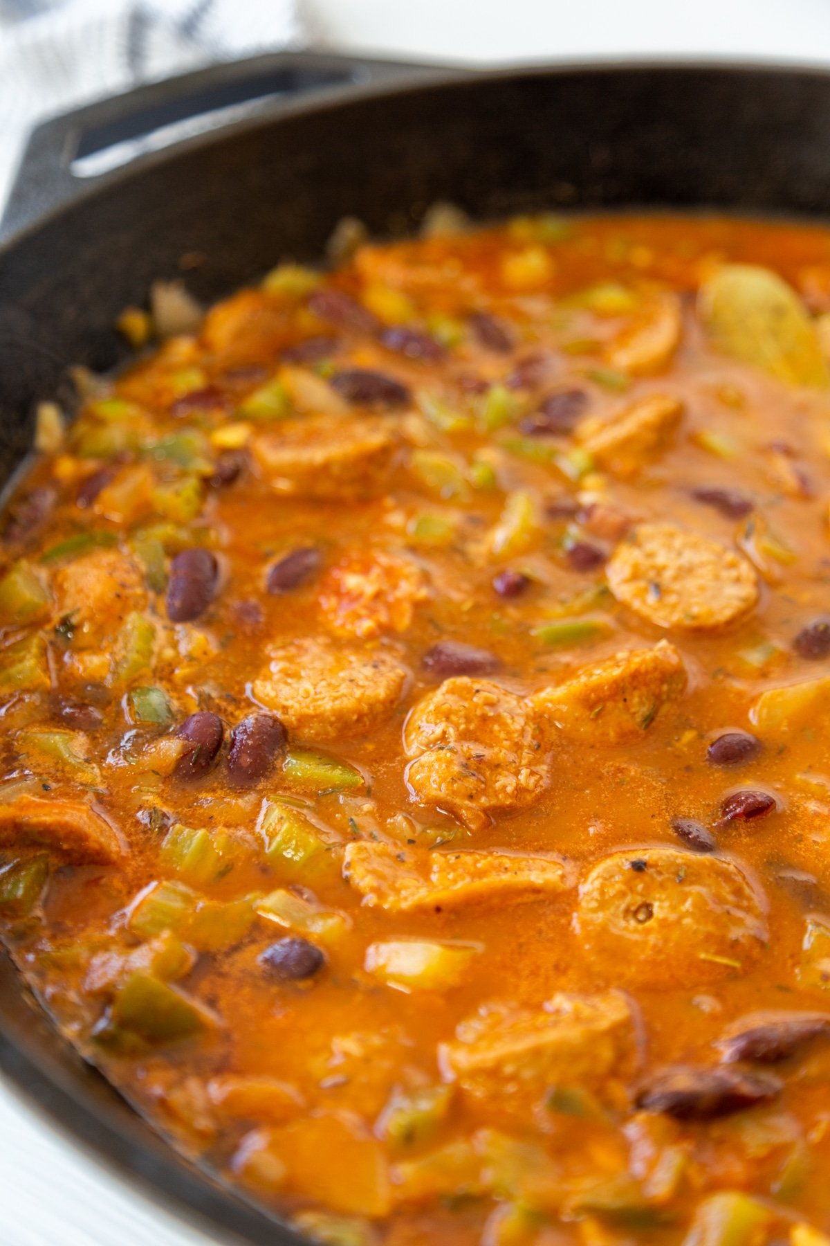 An iron skillet with red beans, spices, broth, and sausage.