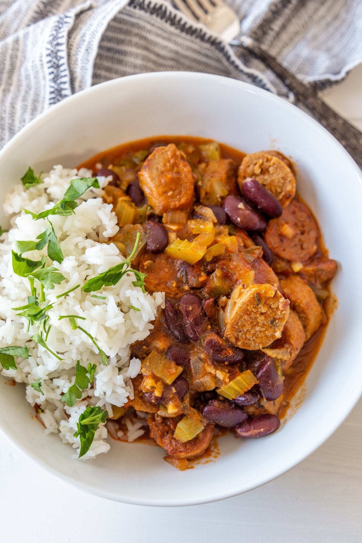 A white bowl filled with red beans and rice with sausage, and garnished with chopped parsley.