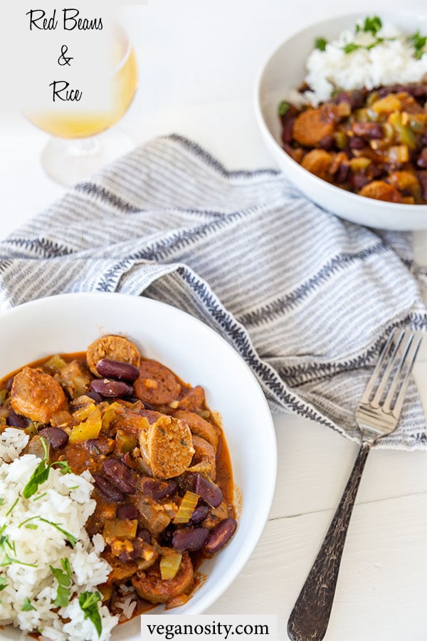 A Pinterest pin for vegan red beans and rice with a picture of 2 white bowls filled with rice and beans and a silver fork and black and white napkin, and a glass of beer.