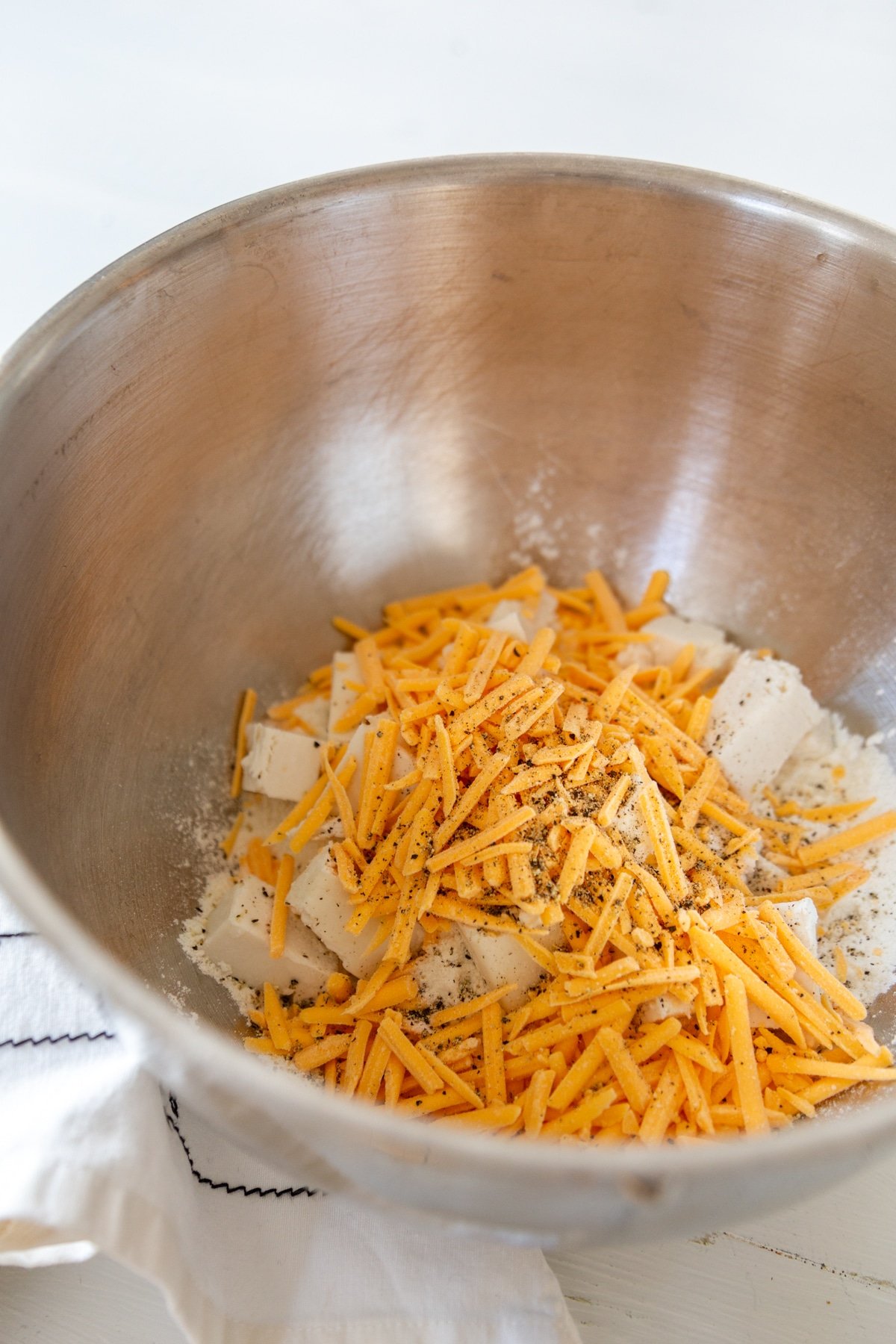 A silver mixing bowl with flour, butter, and cheddar cheese shreds.