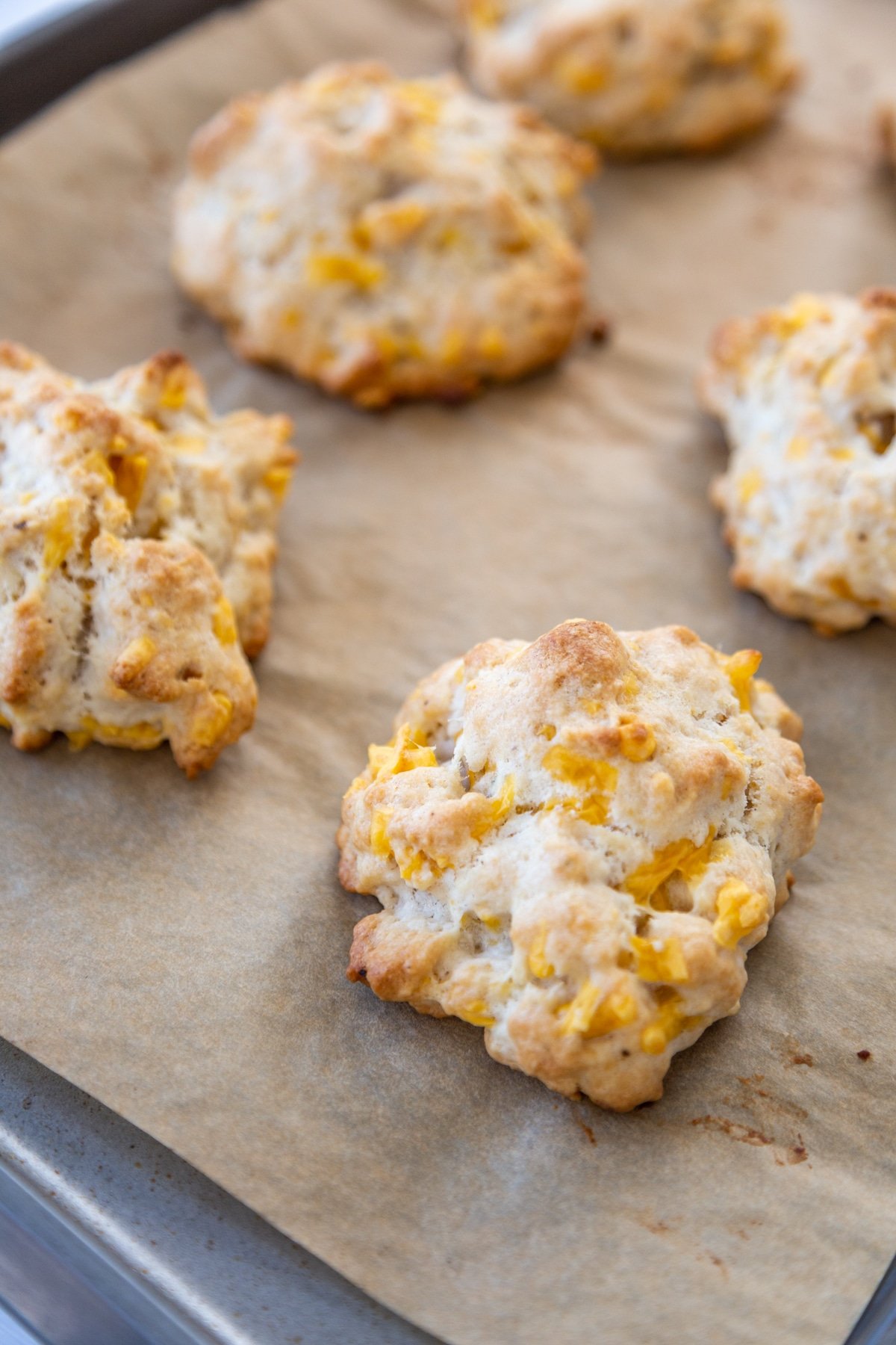 Cheddar drop biscuits on a parchment paper lined baking sheet.