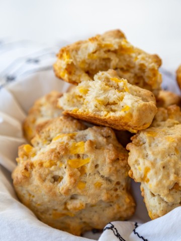 A basket of cheddar drop biscuits with the top biscuit torn in half to show the melted cheese and the texture.