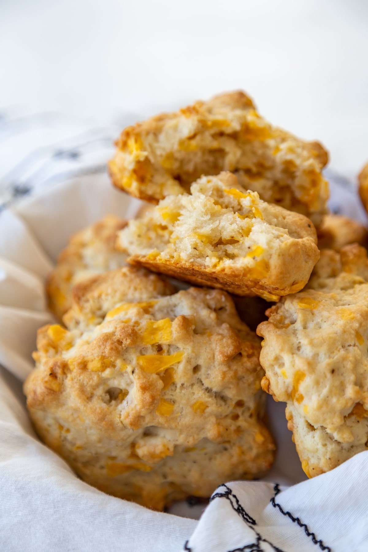 A basket of cheddar drop biscuits with the top biscuit torn in half to show the melted cheese and the texture.