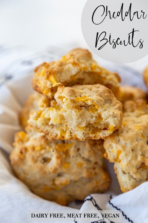 A Pinterest pin for vegan cheddar drop biscuits in a basket with the top biscuit torn in half to show the center.