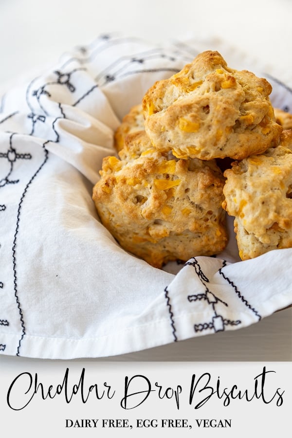 A Pinterest pin for vegan cheddar drop biscuits with a pile of the biscuits in a basket with a white and black napkin.